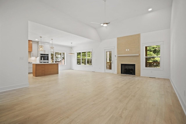 unfurnished living room featuring a large fireplace, light hardwood / wood-style floors, ceiling fan, and a healthy amount of sunlight