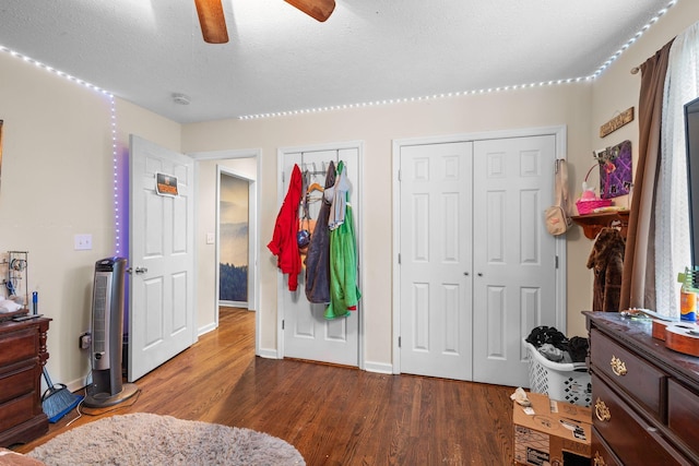 bedroom with a textured ceiling, ceiling fan, dark wood-type flooring, and two closets