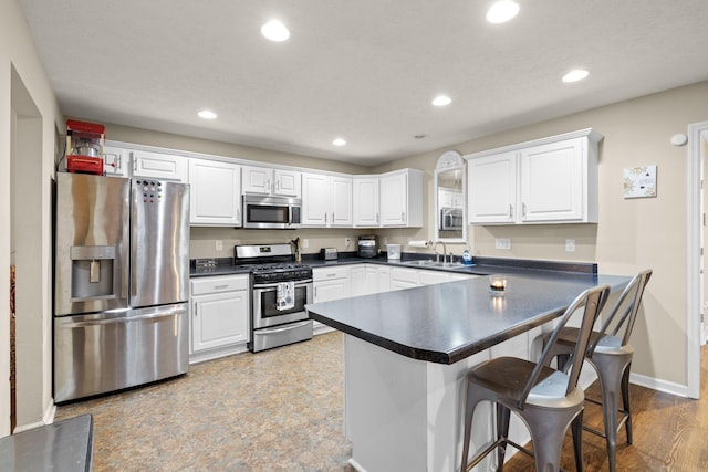 kitchen with white cabinetry, sink, kitchen peninsula, a breakfast bar, and appliances with stainless steel finishes