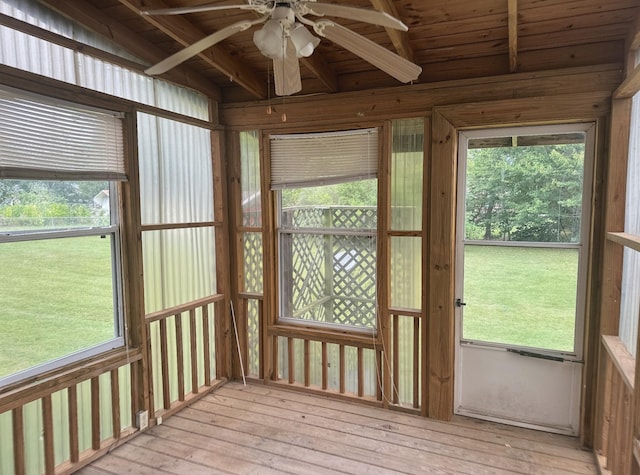 unfurnished sunroom with beamed ceiling, plenty of natural light, ceiling fan, and wooden ceiling