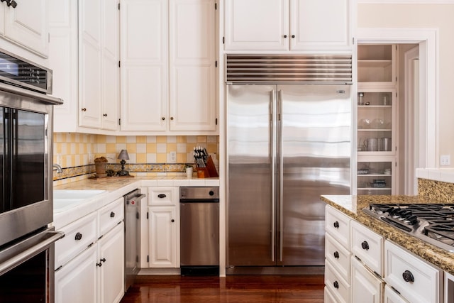 kitchen with white cabinets, backsplash, stainless steel appliances, and dark wood-type flooring