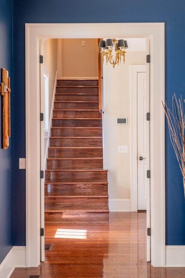 staircase with wood-type flooring and an inviting chandelier