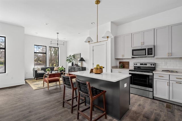 kitchen with appliances with stainless steel finishes, a breakfast bar, dark wood-type flooring, pendant lighting, and a center island