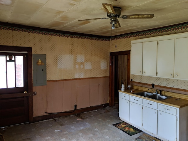 kitchen with wood walls, electric panel, sink, ceiling fan, and white cabinetry