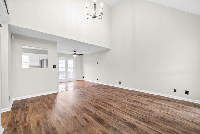 unfurnished living room with french doors, high vaulted ceiling, ceiling fan with notable chandelier, and hardwood / wood-style flooring