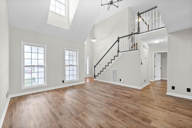 unfurnished living room featuring hardwood / wood-style floors, an inviting chandelier, and high vaulted ceiling