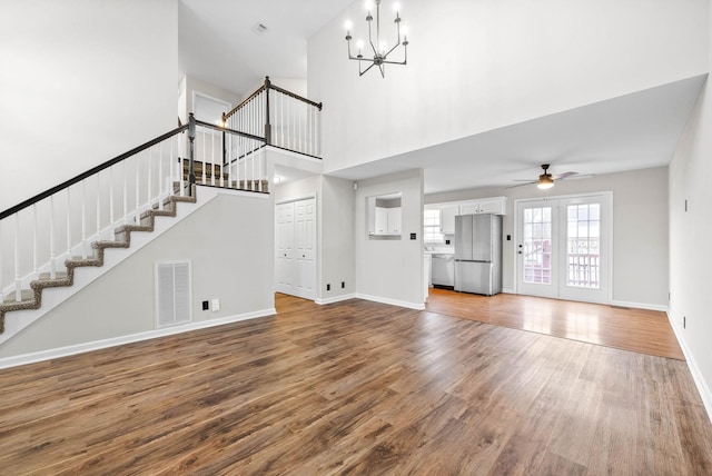 unfurnished living room with ceiling fan with notable chandelier, wood-type flooring, and a towering ceiling