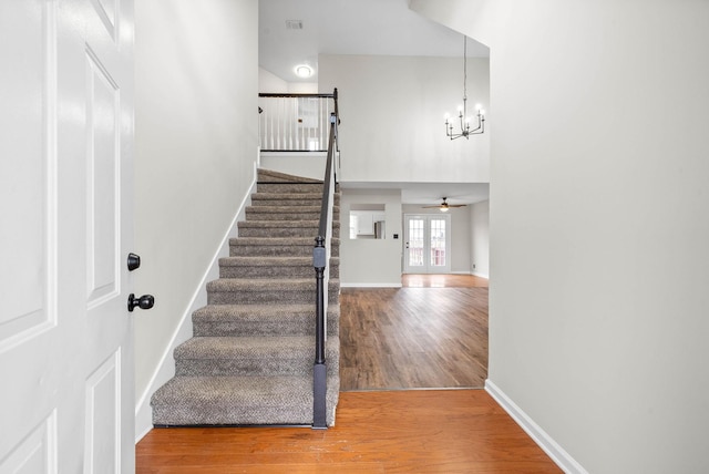 stairs featuring french doors, ceiling fan with notable chandelier, and hardwood / wood-style flooring