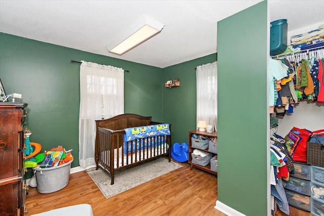 bedroom featuring a crib, wood-type flooring, and multiple windows