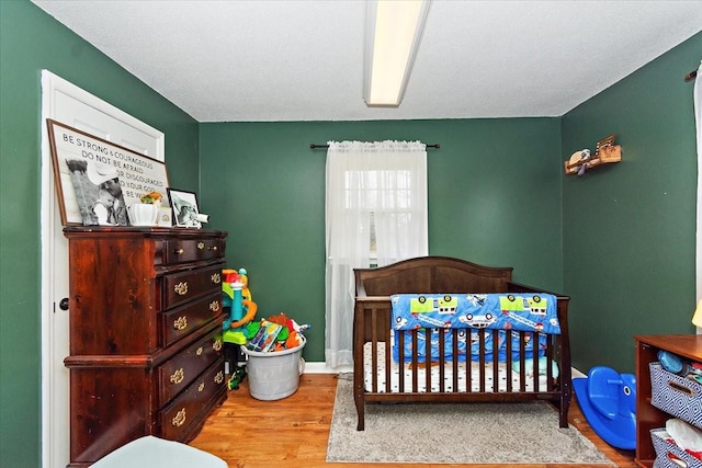 bedroom with wood-type flooring, a textured ceiling, and a nursery area