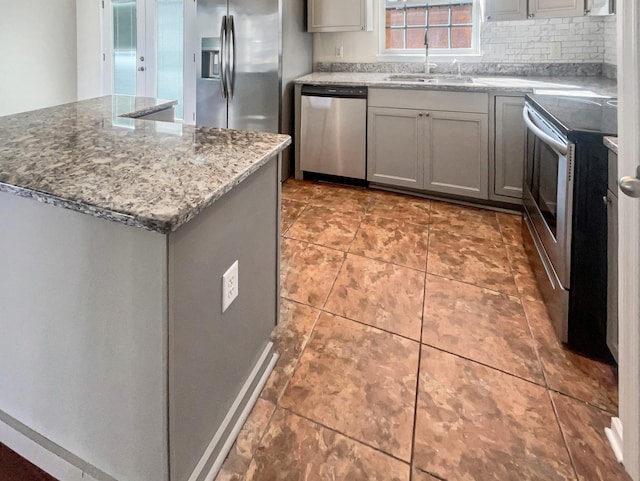 kitchen with gray cabinetry, a center island, sink, light stone countertops, and appliances with stainless steel finishes