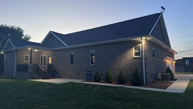 back house at dusk featuring a lawn and cooling unit