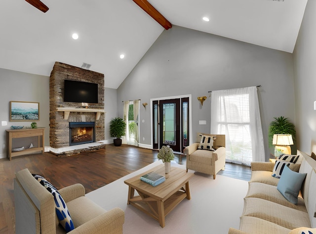 living room featuring beamed ceiling, wood-type flooring, high vaulted ceiling, and a stone fireplace