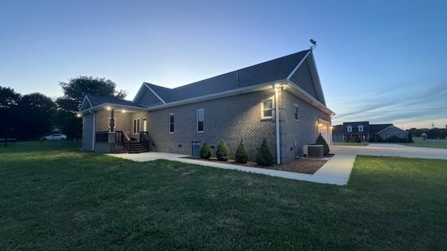 back house at dusk featuring a yard and central air condition unit