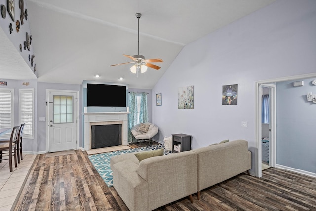 living room with hardwood / wood-style floors, ceiling fan, high vaulted ceiling, and a tile fireplace