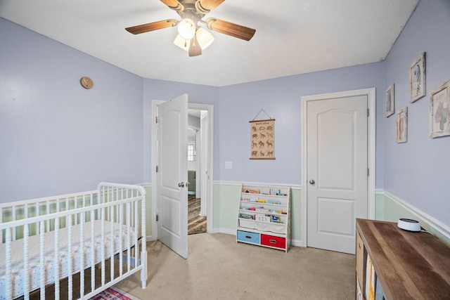 carpeted bedroom featuring a textured ceiling, a nursery area, and ceiling fan