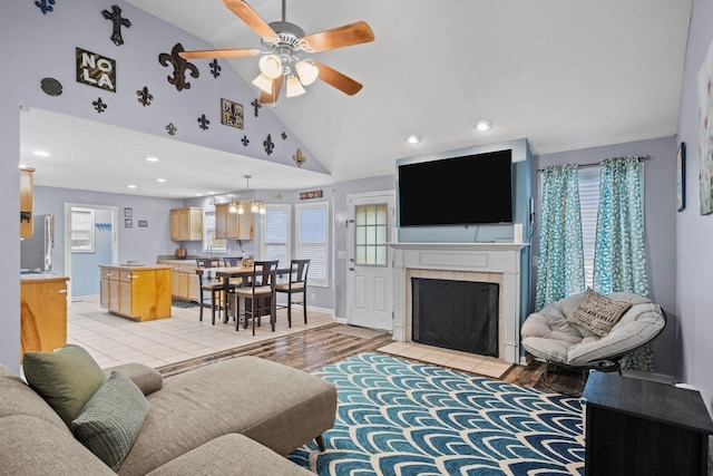 living room featuring a fireplace, high vaulted ceiling, ceiling fan with notable chandelier, and light wood-type flooring