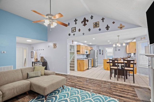 living room featuring ceiling fan with notable chandelier, high vaulted ceiling, and light hardwood / wood-style flooring