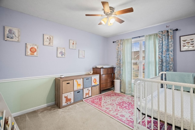 bedroom featuring ceiling fan, light colored carpet, and a crib