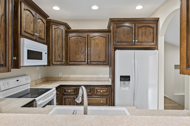 kitchen with dark brown cabinets, sink, white appliances, and hardwood / wood-style flooring