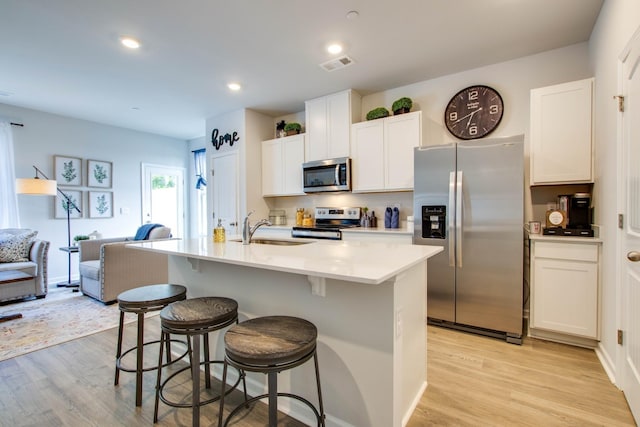 kitchen with light hardwood / wood-style floors, white cabinetry, stainless steel appliances, and an island with sink