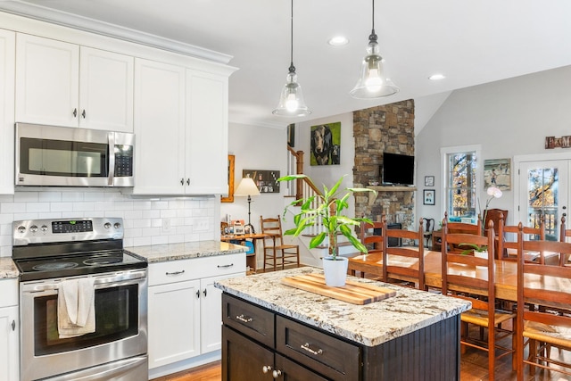 kitchen with white cabinets, decorative backsplash, light stone countertops, appliances with stainless steel finishes, and a kitchen island