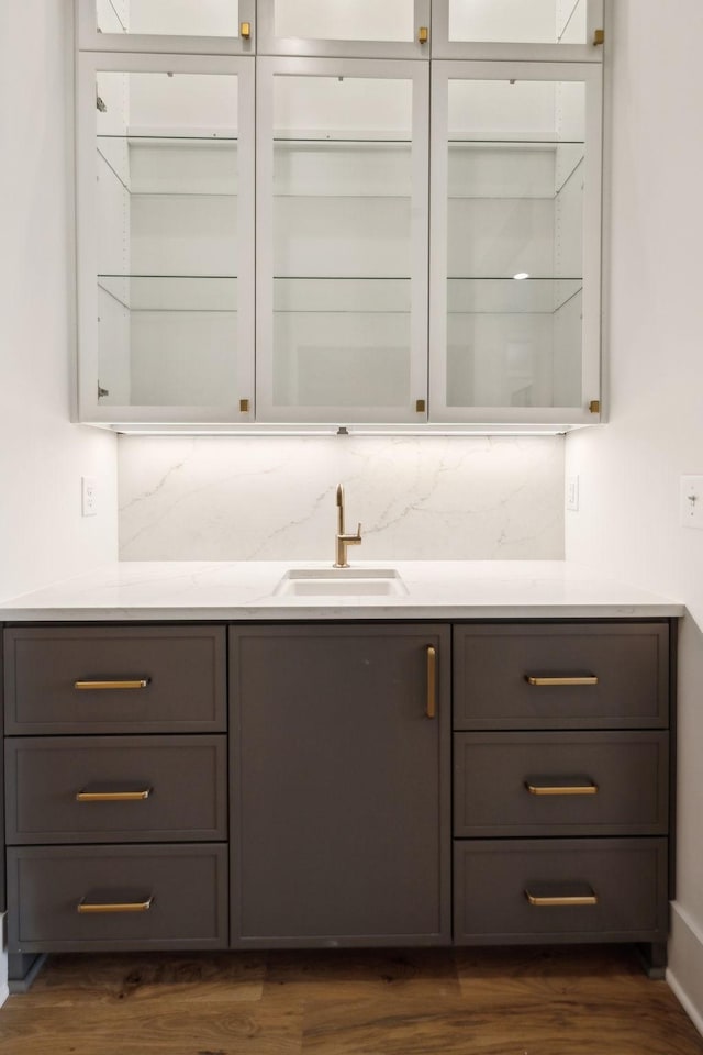 bar with sink, dark hardwood / wood-style floors, light stone countertops, and tasteful backsplash