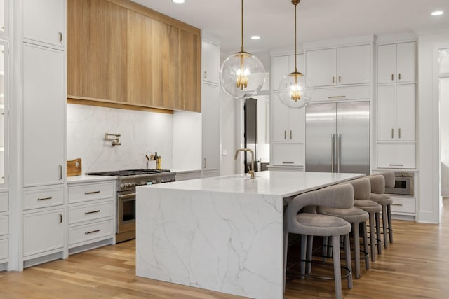 kitchen with white cabinets, light stone counters, light hardwood / wood-style flooring, high end appliances, and a kitchen island with sink