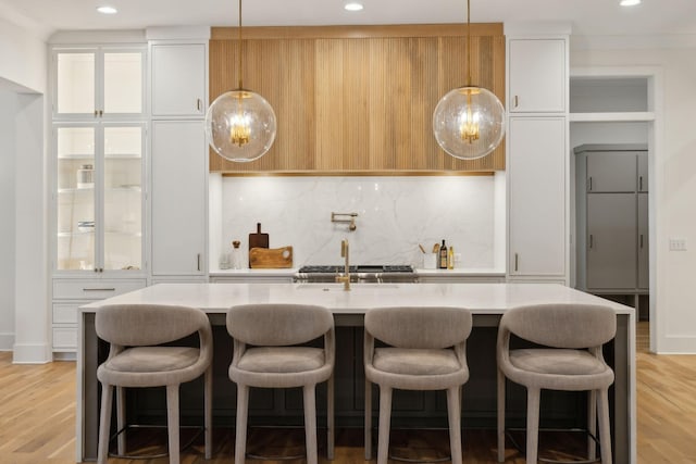 kitchen featuring white cabinets, light stone counters, tasteful backsplash, an island with sink, and light hardwood / wood-style flooring