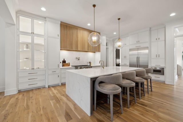 kitchen featuring white cabinets, light hardwood / wood-style floors, light stone countertops, and a center island with sink