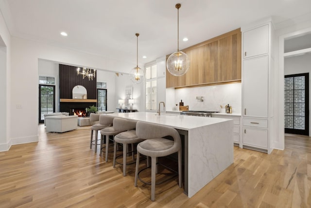 kitchen featuring a large fireplace, an island with sink, pendant lighting, decorative backsplash, and white cabinets