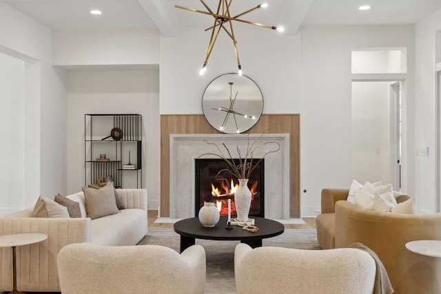 living room featuring beam ceiling, a premium fireplace, light wood-type flooring, and an inviting chandelier