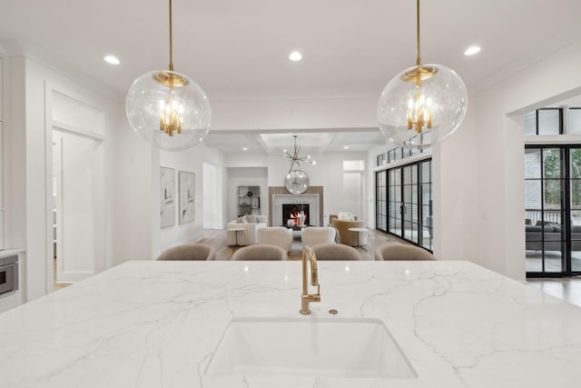 kitchen featuring sink, decorative light fixtures, a high end fireplace, and light stone countertops