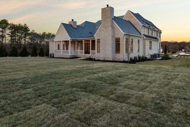 back house at dusk with a lawn, cooling unit, and covered porch