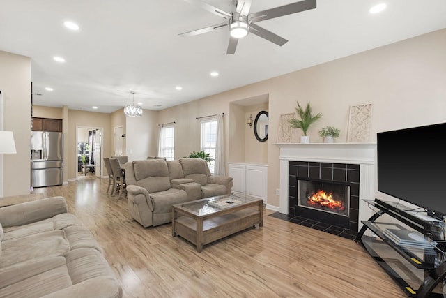 living room featuring ceiling fan with notable chandelier, light wood-type flooring, and a tiled fireplace