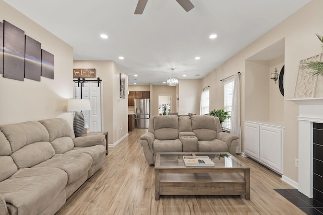 living room featuring a barn door, ceiling fan with notable chandelier, and light wood-type flooring