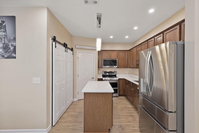 kitchen featuring stainless steel appliances, a barn door, decorative light fixtures, light hardwood / wood-style flooring, and a center island