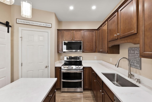 kitchen with appliances with stainless steel finishes, sink, pendant lighting, a barn door, and light hardwood / wood-style flooring