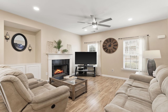 living room with ceiling fan, a fireplace, and light hardwood / wood-style floors