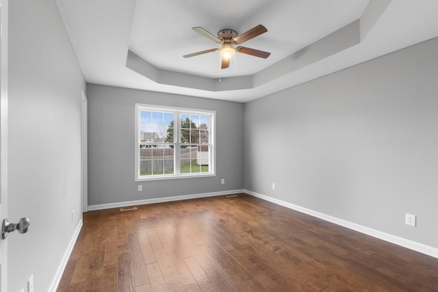 spare room with a tray ceiling, ceiling fan, and dark wood-type flooring