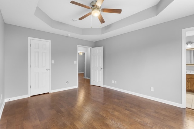 unfurnished bedroom featuring a raised ceiling, connected bathroom, ceiling fan, and dark hardwood / wood-style flooring