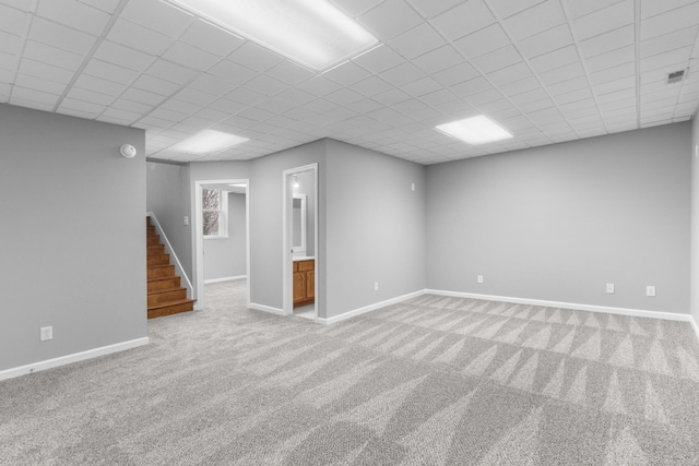 basement featuring a paneled ceiling and light colored carpet