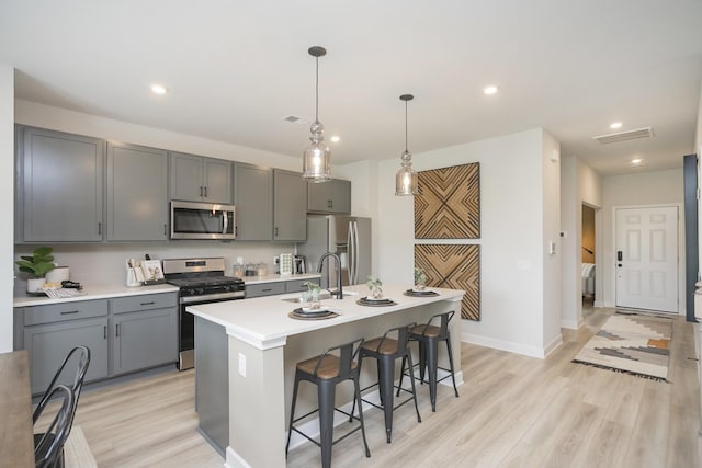 kitchen featuring sink, light hardwood / wood-style flooring, gray cabinets, a kitchen island with sink, and appliances with stainless steel finishes