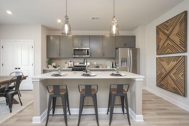 kitchen with gray cabinets, an island with sink, stainless steel appliances, and light hardwood / wood-style floors