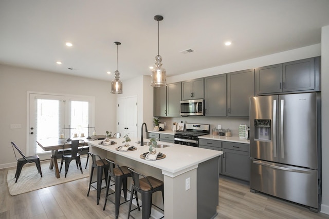 kitchen with sink, stainless steel appliances, an island with sink, light hardwood / wood-style floors, and decorative light fixtures