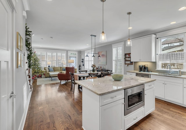 kitchen with stainless steel microwave, sink, light hardwood / wood-style flooring, decorative light fixtures, and white cabinets