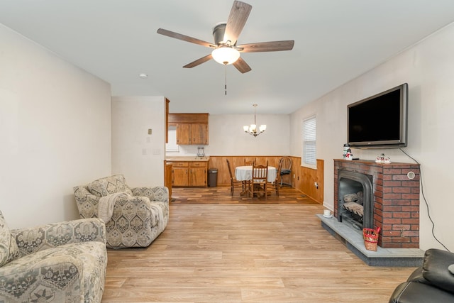 living room with ceiling fan with notable chandelier, light wood-type flooring, and wooden walls