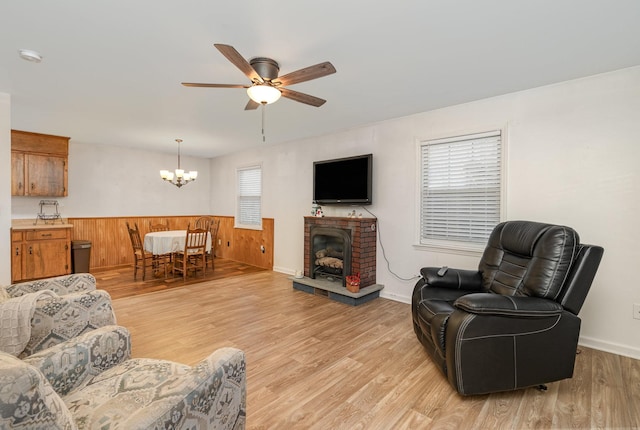 living room featuring a brick fireplace, ceiling fan with notable chandelier, light hardwood / wood-style flooring, and wooden walls