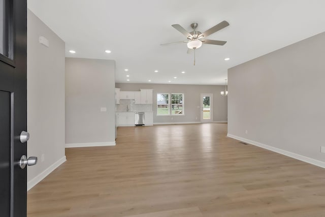 unfurnished living room featuring ceiling fan with notable chandelier and light wood-type flooring