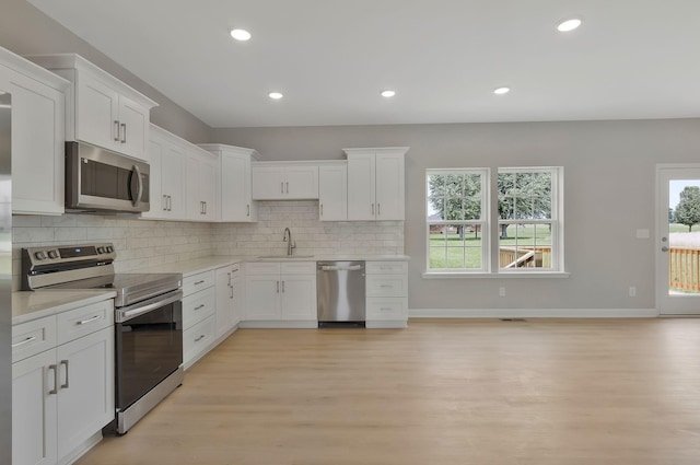 kitchen featuring decorative backsplash, sink, light wood-type flooring, appliances with stainless steel finishes, and white cabinets